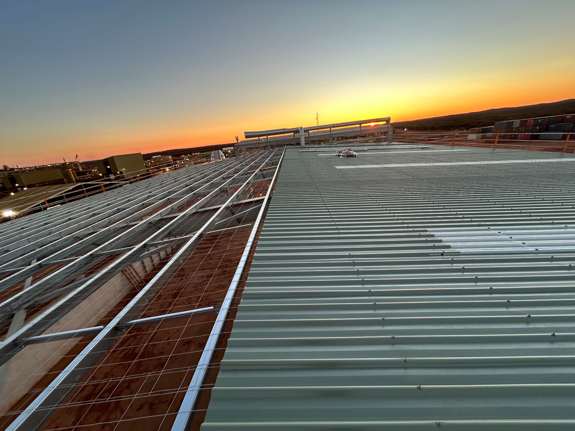 Crew installing standing seam metal roof on an industrial facility in regional WA at dusk